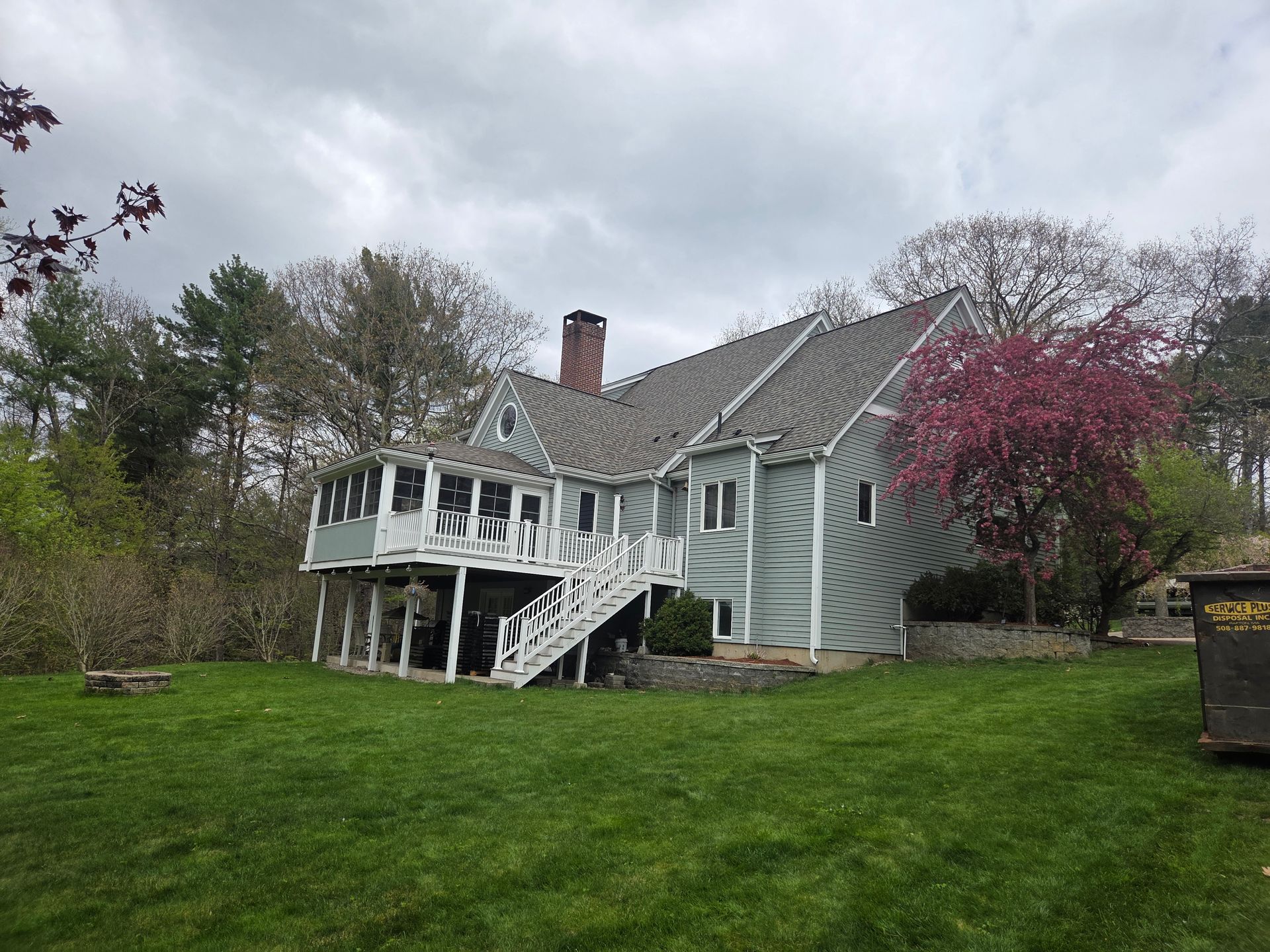 Gray house with white porch and stairs, set on a green lawn with trees and cloudy sky