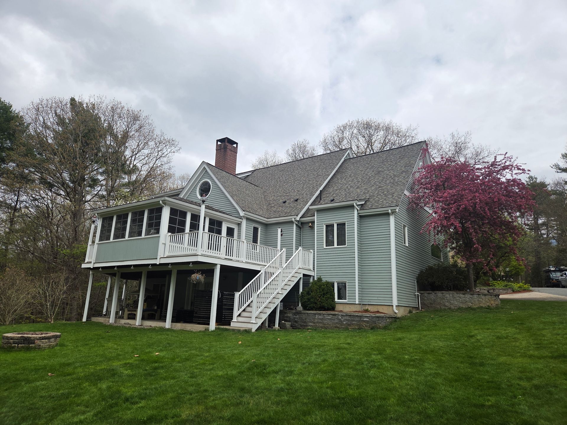 White farmhouse-style house with porch and stairs on a green lawn under cloudy skies