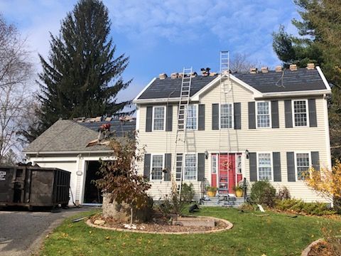 Two-story beige house with red front door, white shutters, and a driveway beside a garage under a blue sky