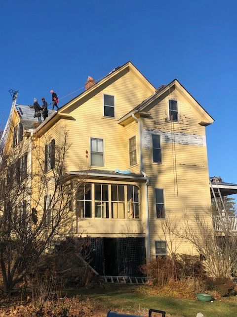 Yellow house with workers on the roof under a clear blue sky