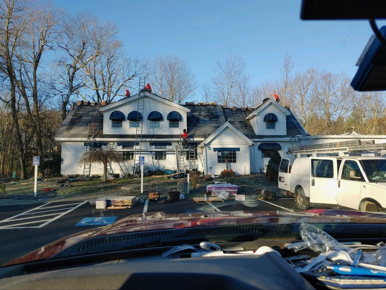 White house with dormer windows and parked vehicles, viewed from a car in a driveway
