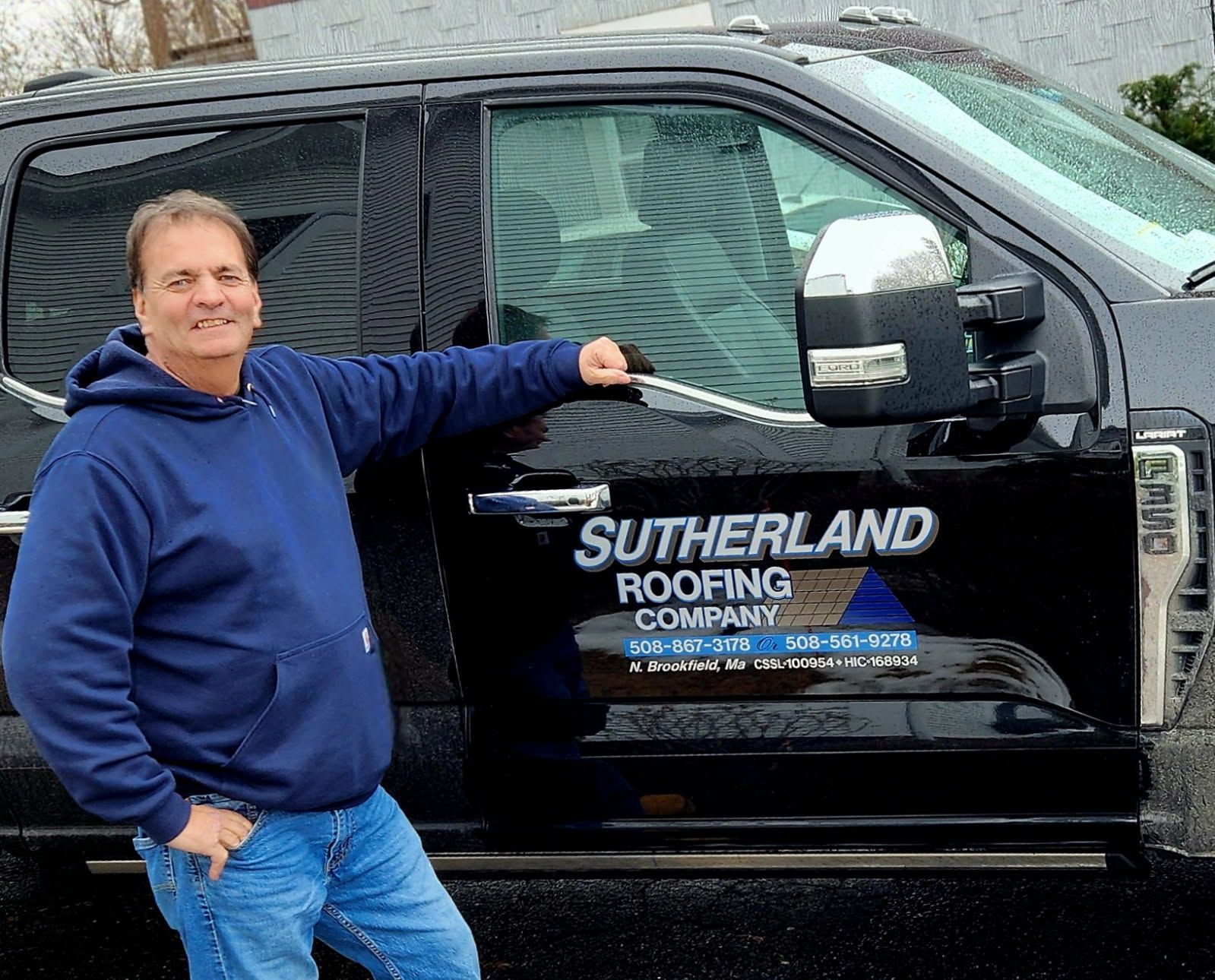 Man in blue hoodie leaning on black Sutherland Roofing Company truck