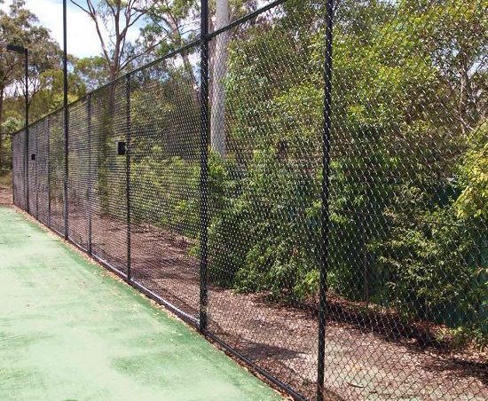 A black chain link fence surrounds a tennis court.