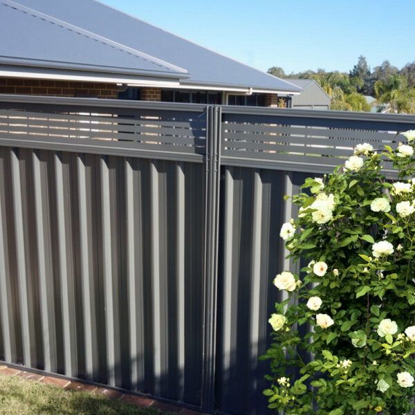 A fence with flowers in front of it and a house in the background.