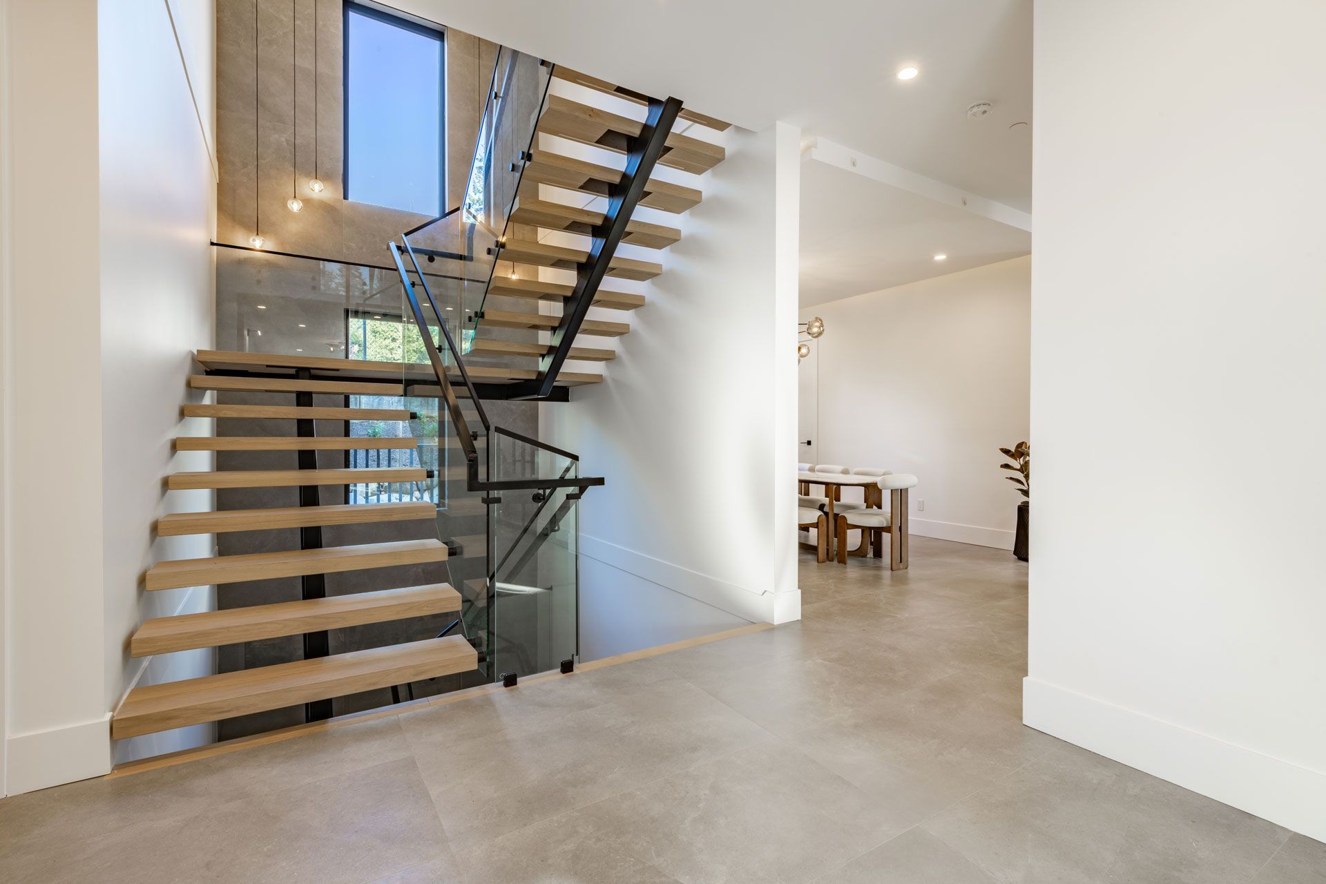 Modern staircase with wooden steps, black railing, and glass panels in a home's entryway.