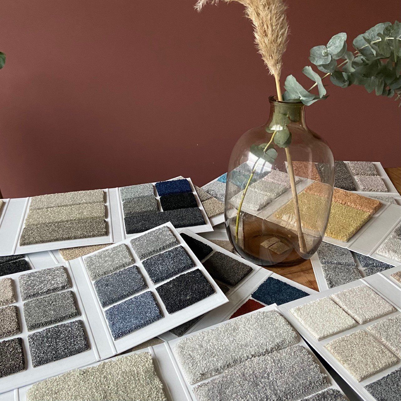 Een vaas met een plant erin staat op een tafel omringd door tapijtmonsters