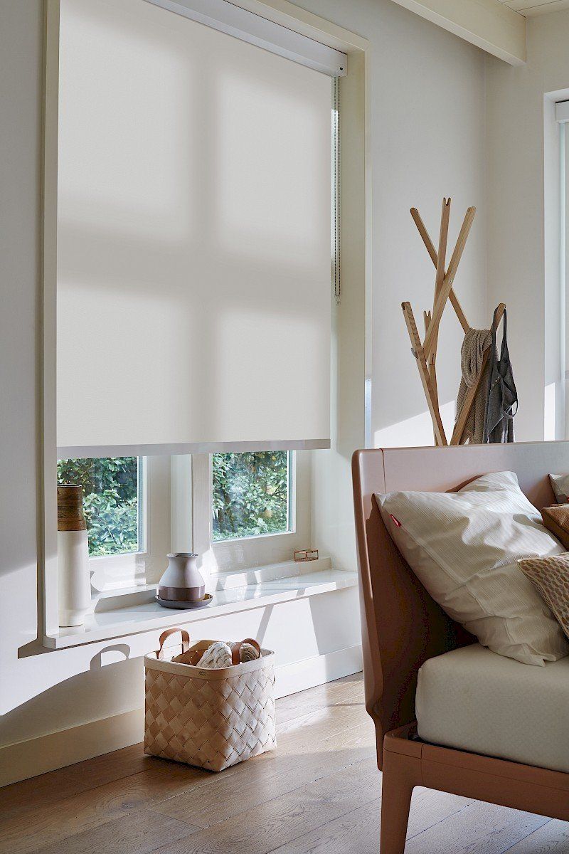 Een woonkamer met een bed en een raam met een wit gordijn.