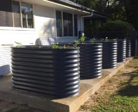 A Metal Planter Filled With Lots of Plants is Sitting on Top of a Lush Green Lawn — Foley's Tanks in Woombye, QLD