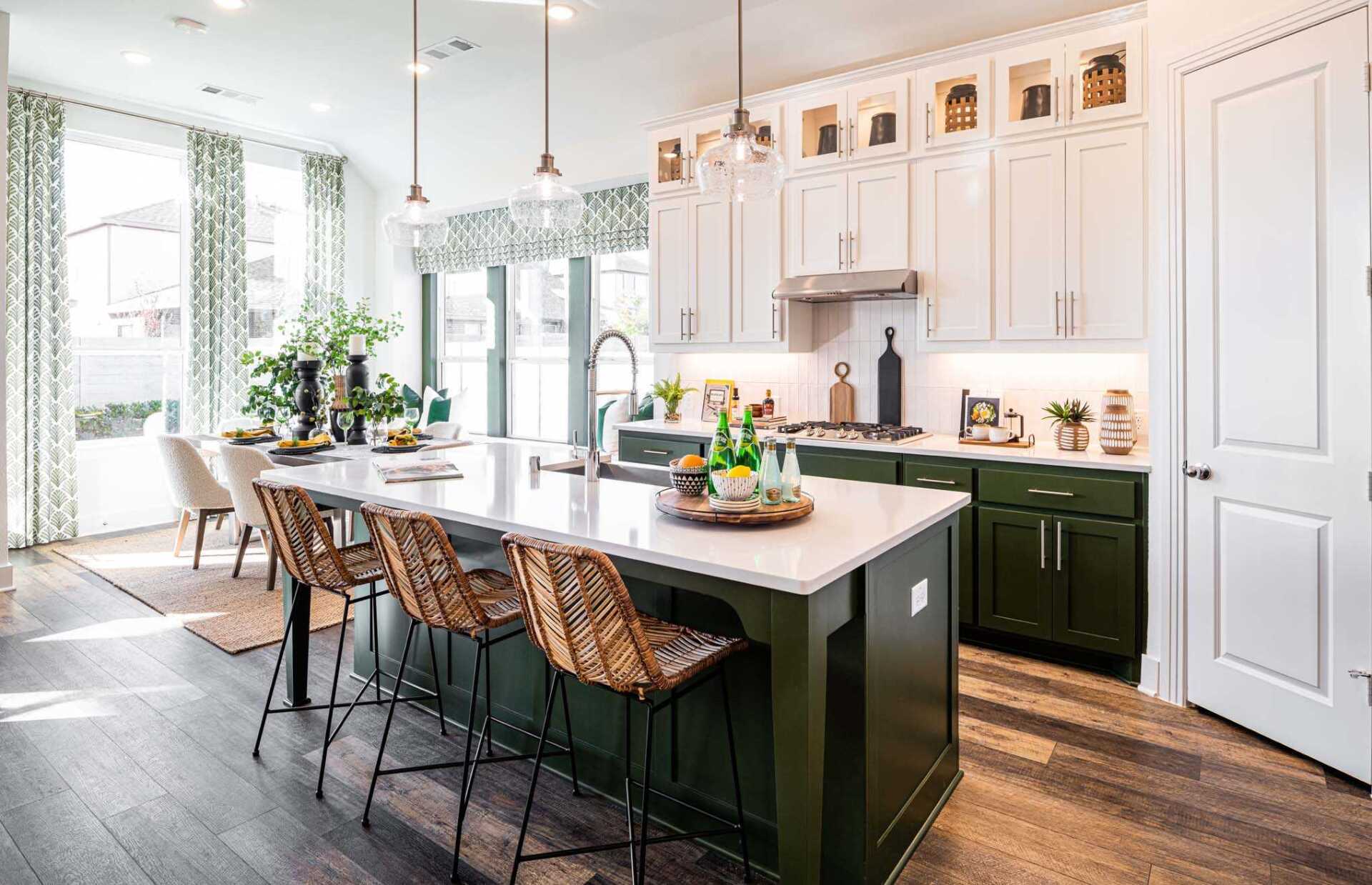 Modern kitchen with white upper cabinets, green lower cabinets, island with woven barstools, and large windows.