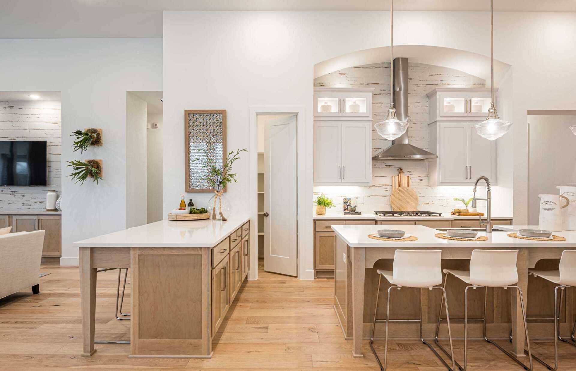 Spacious kitchen with two islands, light wood cabinets, white countertops, and wood floors.