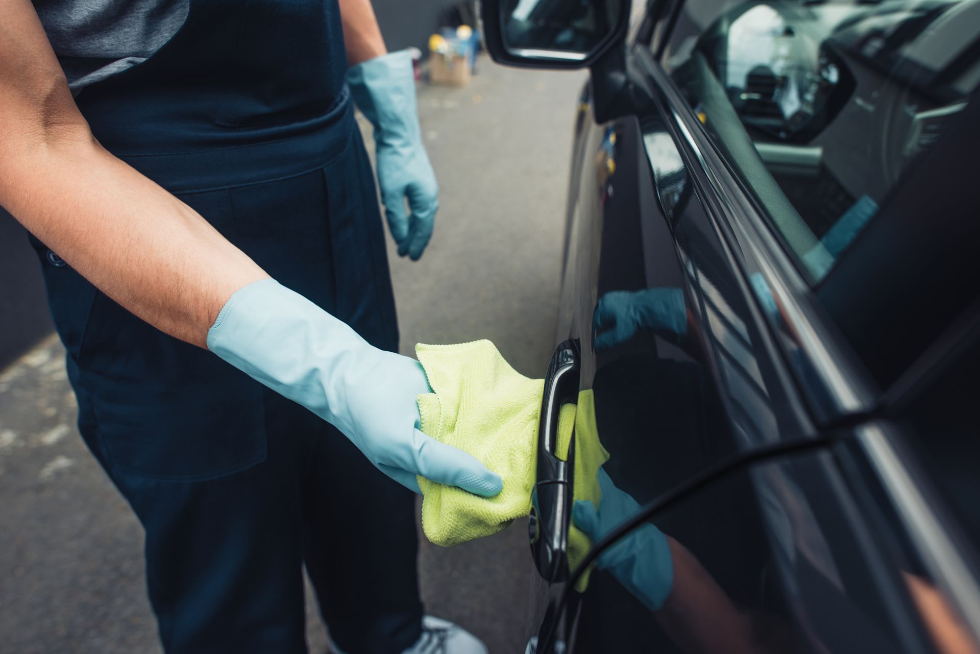 A person wearing gloves is cleaning a car with a cloth.