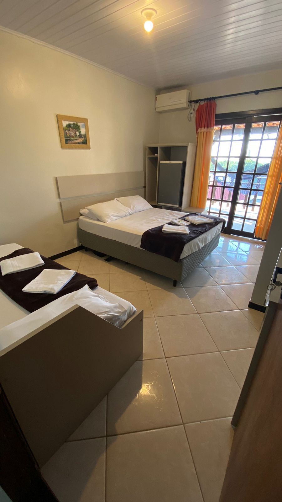 Quarto de hotel com duas camas, toalhas, janela com cortinas e pequeno armário.