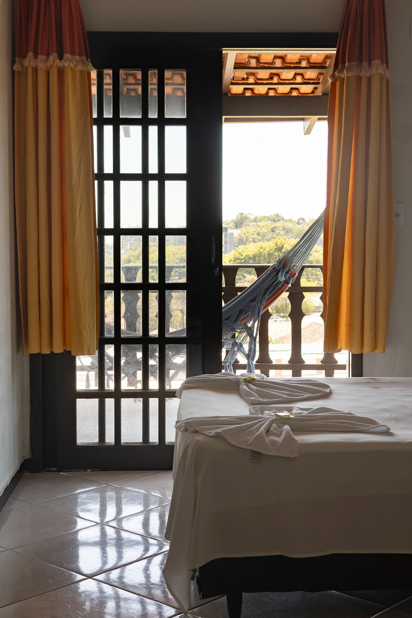 Quarto com porta aberta para uma varanda; cama, cortinas e rede visíveis.