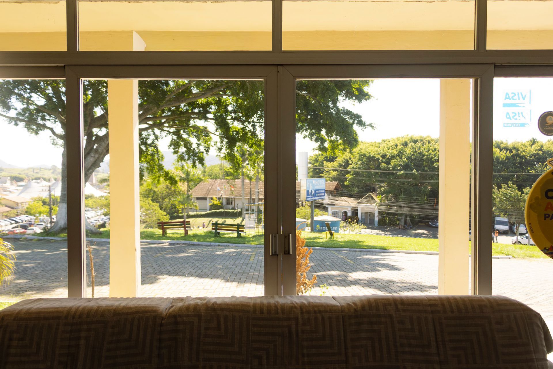 Vista através de portas de vidro: um parque com árvores, casas e bancos.