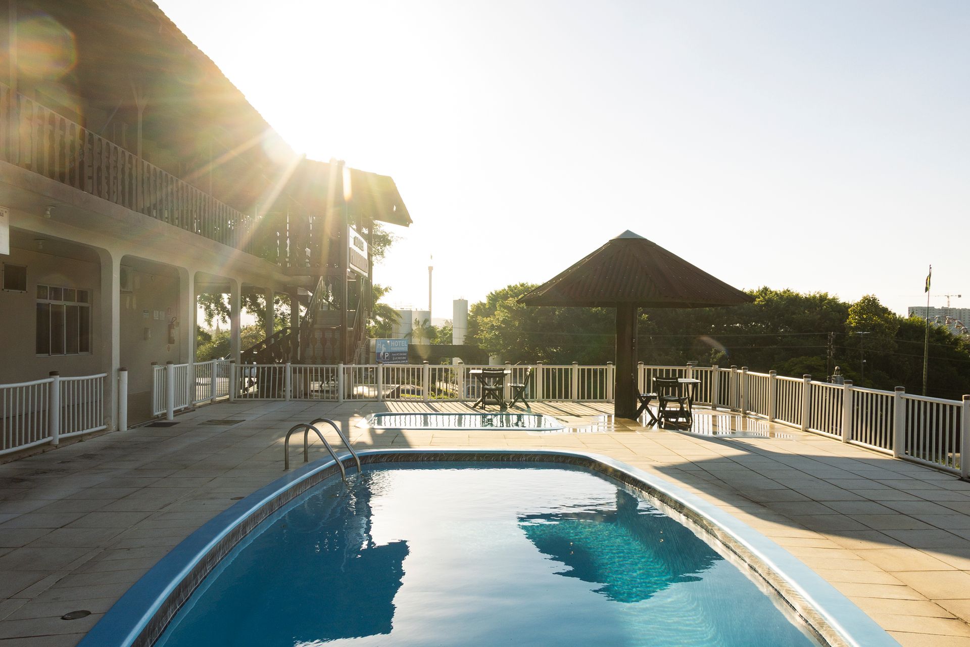 Área da piscina com piscina retangular, cabana, construção e muita luz solar.