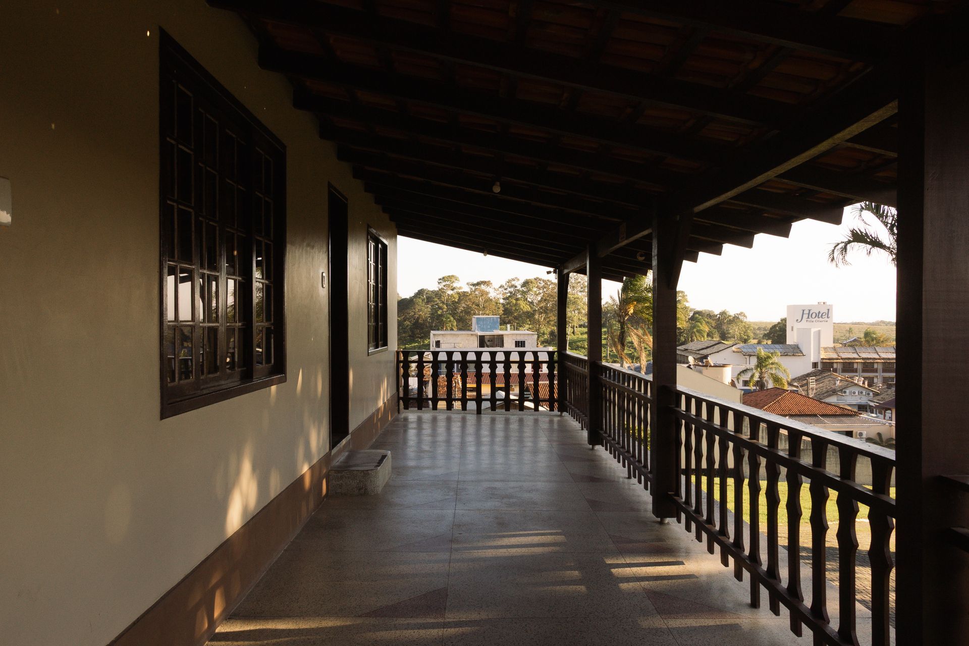 Varanda externa coberta com grades de madeira e vista para os prédios ao longe.