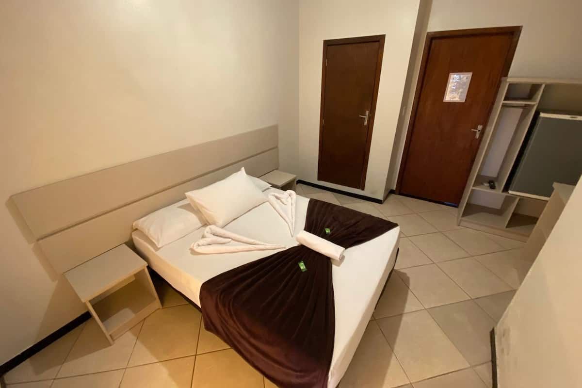 Quarto de hotel com cama, mesa de cabeceira, guarda-roupa e portas fechadas.