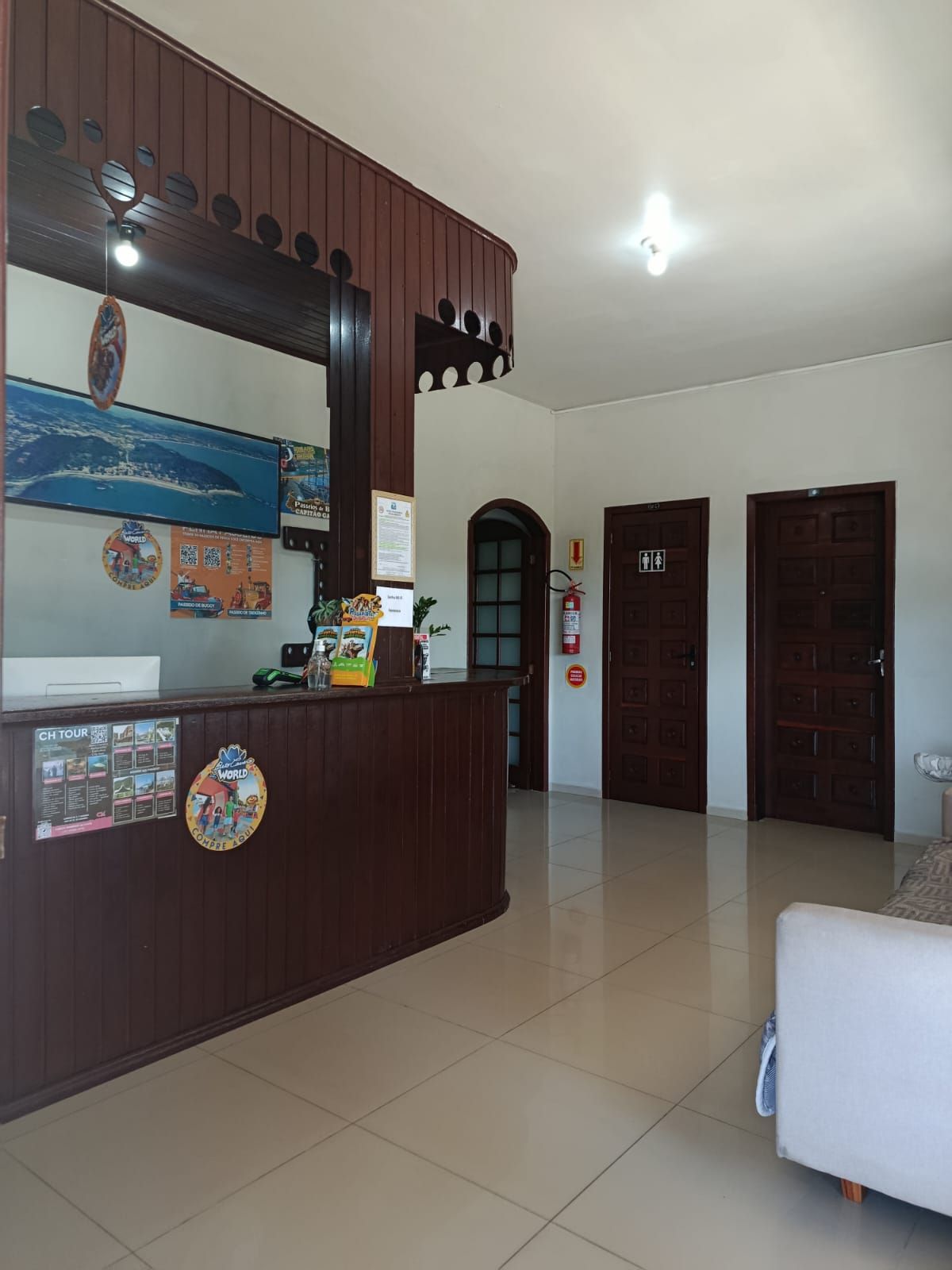 Área de recepção do hotel com balcão de madeira escura, paredes brancas e três portas.