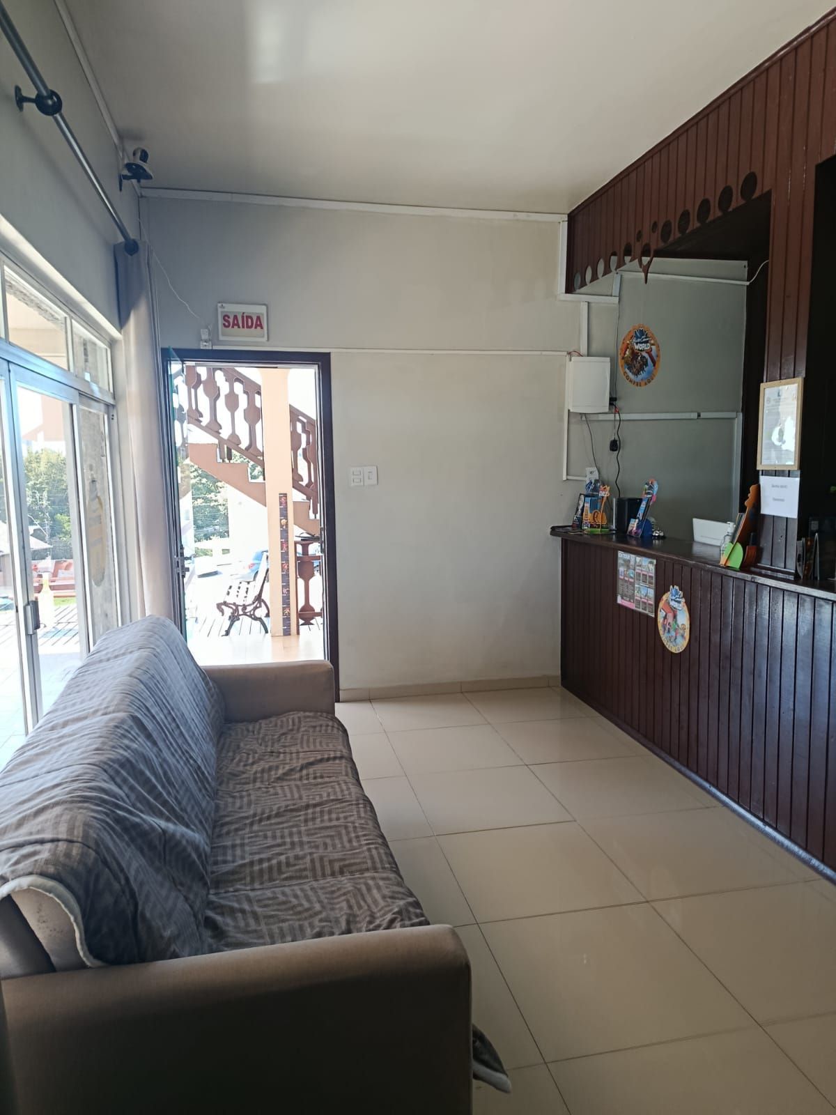 Área de recepção com sofá, mesa e porta para o exterior, em tons de branco e marrom.