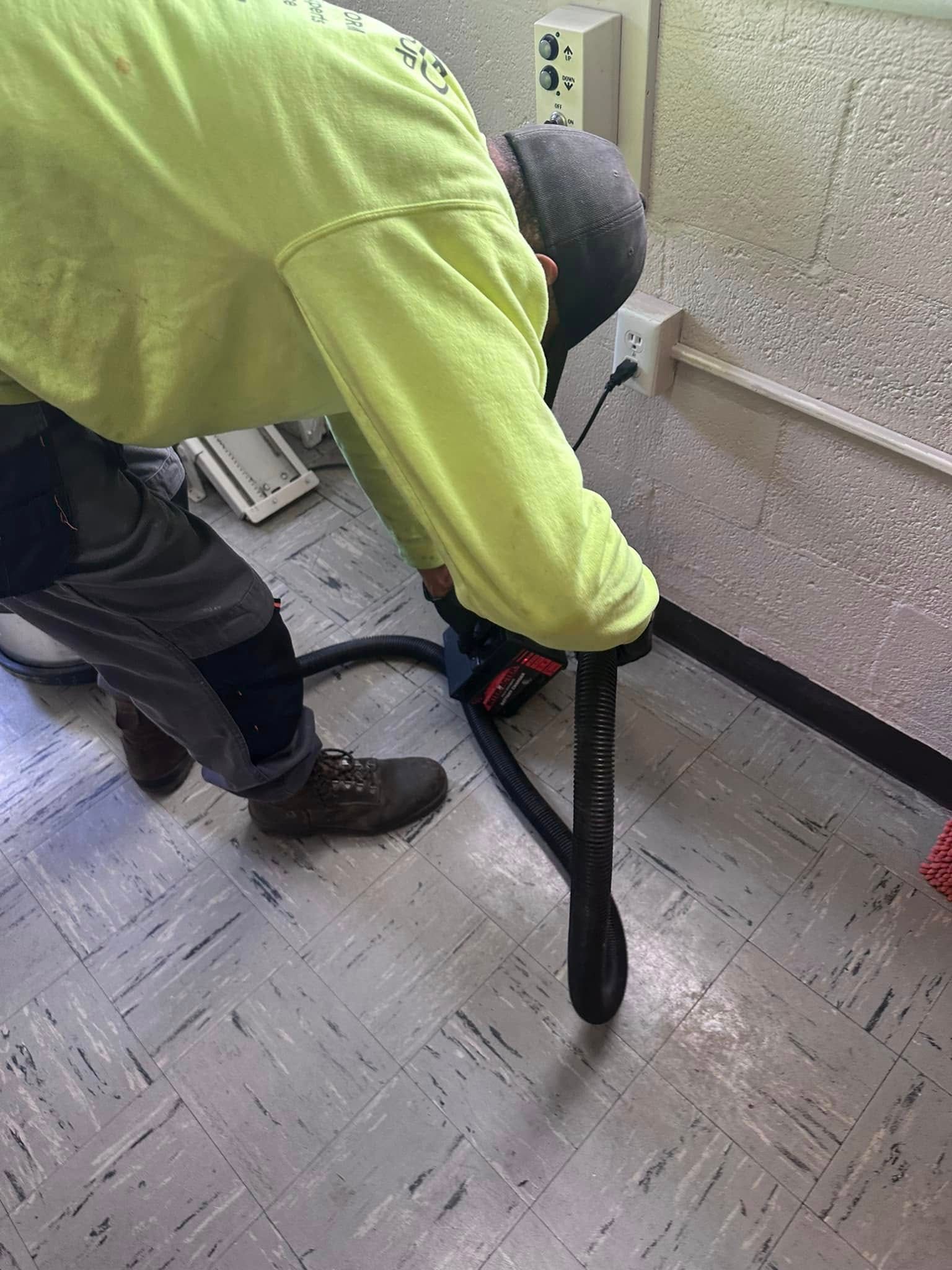 Person in yellow shirt vacuuming a floor. A black vacuum hose is visible.