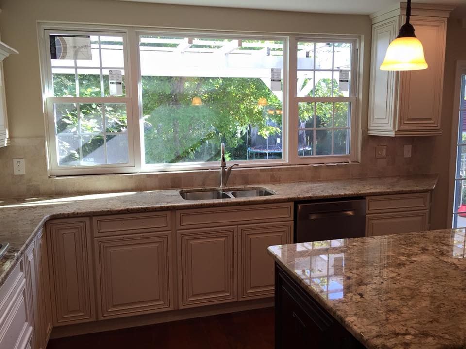 Kitchen with cream cabinets, granite countertops, and a large window overlooking a yard.