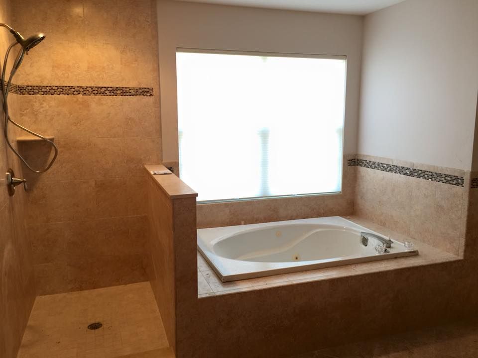 Bathroom with tiled walls, shower, and a built-in tub under a frosted window.