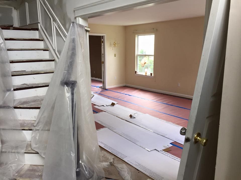 Interior view of a home renovation in progress: stairs, plastic covering, flooring materials, doorway into a room with a window.