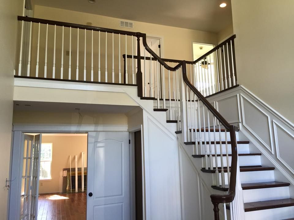 Two-story entry hall with staircase and balcony, white and brown banisters, wood floors, and off-white walls.