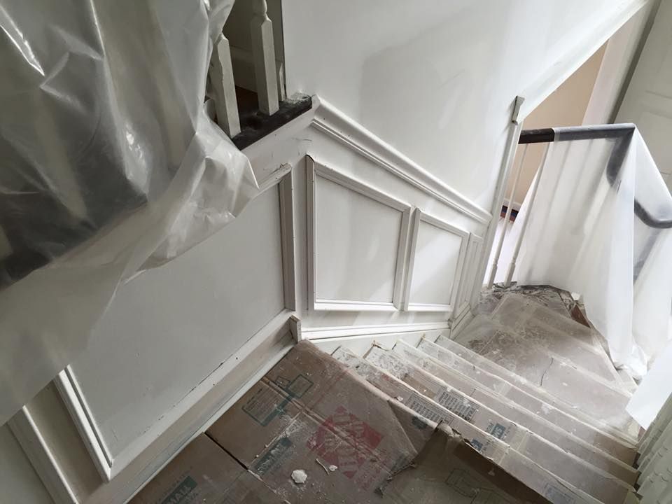 Newly painted white stairwell with paneling, covered with plastic sheeting for protection.