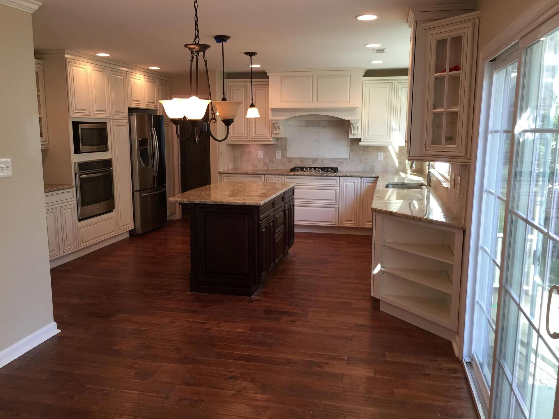 Spacious kitchen with dark wood floors, white cabinets, and a brown island with a granite countertop.