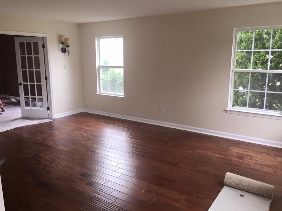 Empty room with wood flooring, beige walls, two windows, and French doors.
