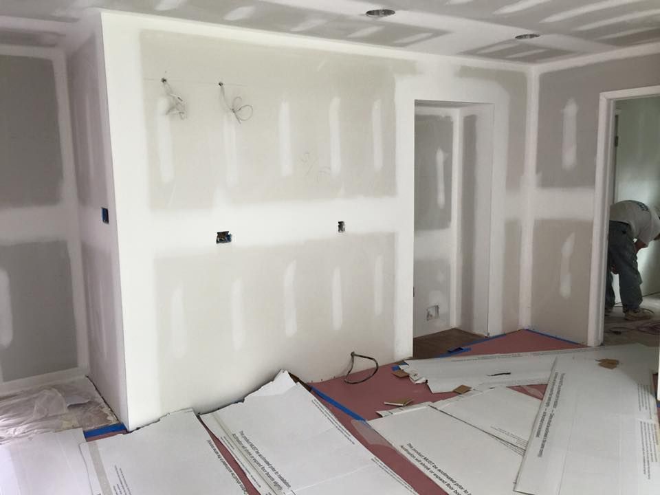 Interior construction of a room: drywall installed, unfinished, with a person working in the doorway.