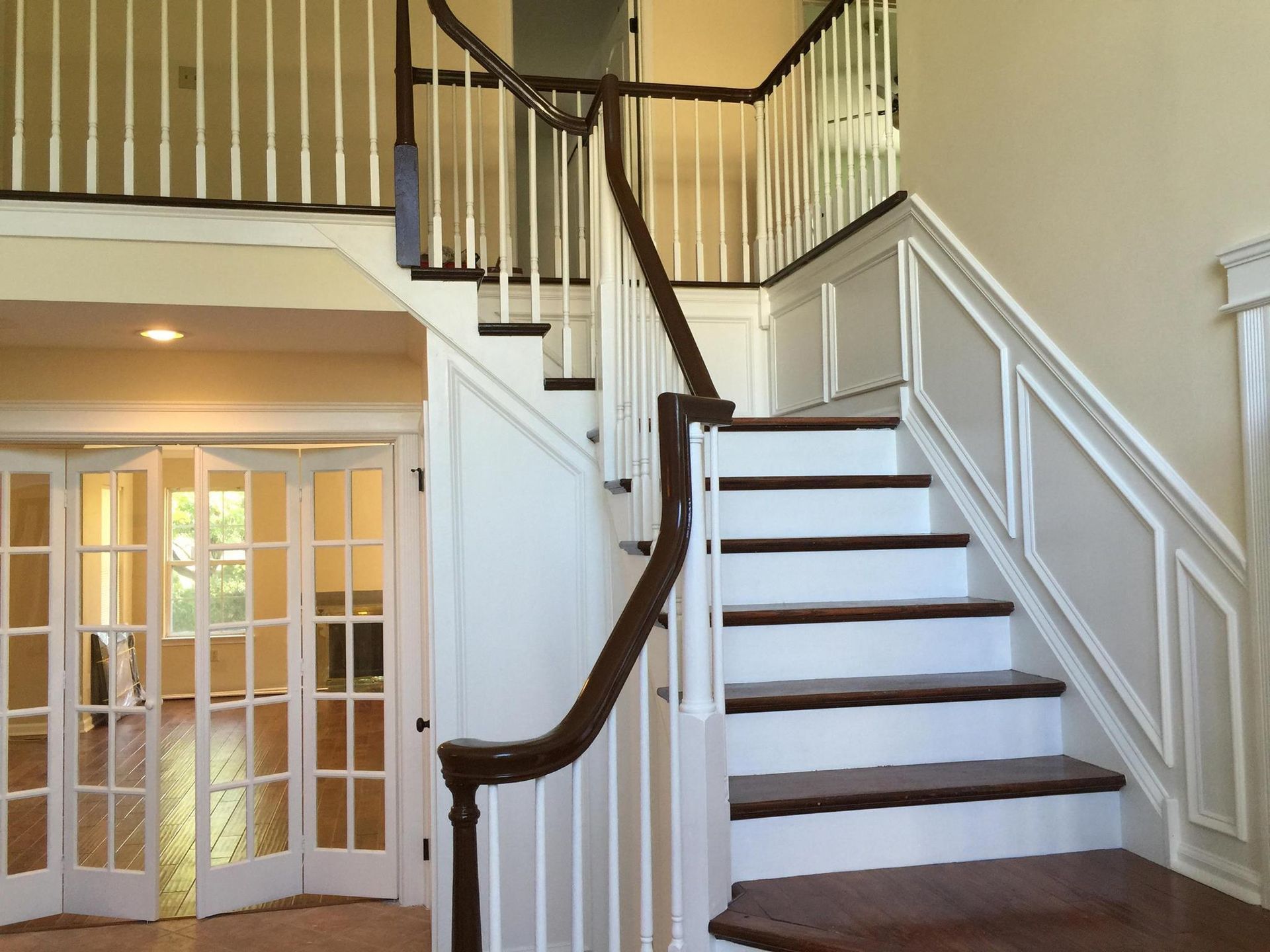 Staircase with wooden steps and white balustrades, leading to a second floor. Large folding doors on the left.