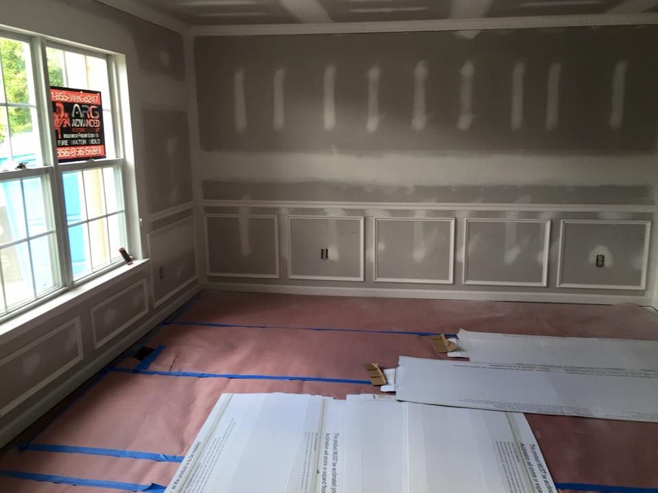 Interior room under construction, with wainscoting and window trim, pink floor covering, and drywall.
