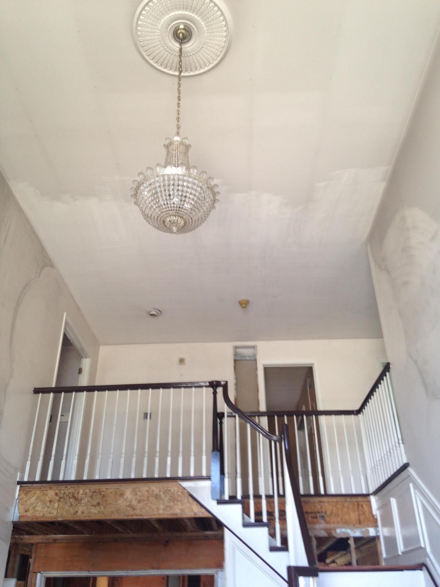 Interior view of a staircase and a chandelier hanging from the ceiling. Staircase has white railings and brown trim.