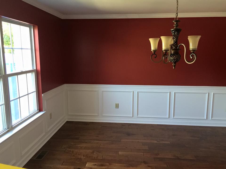 Dining room with red walls, white wainscoting, a window, hardwood floor, and a chandelier.