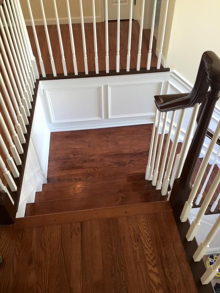 Staircase with wooden steps and railing, leading downward. White and brown trim, hardwood floor.