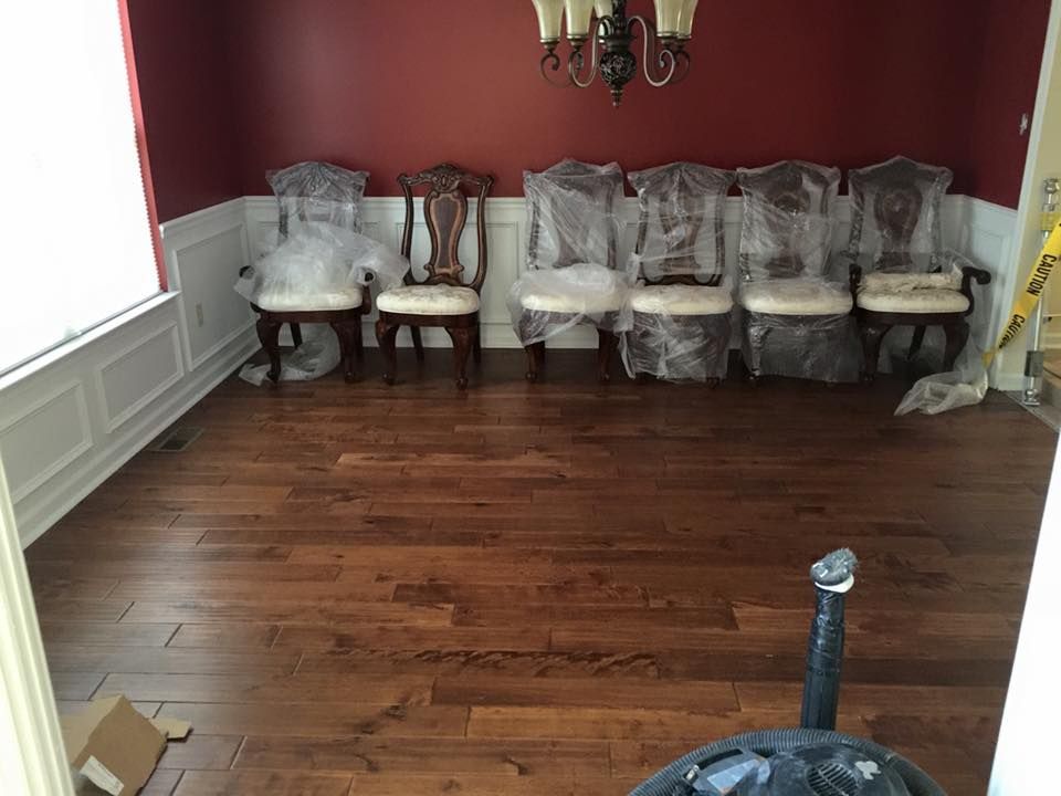 Dining room with dark wood floors, red wall, white wainscoting, and six covered chairs.