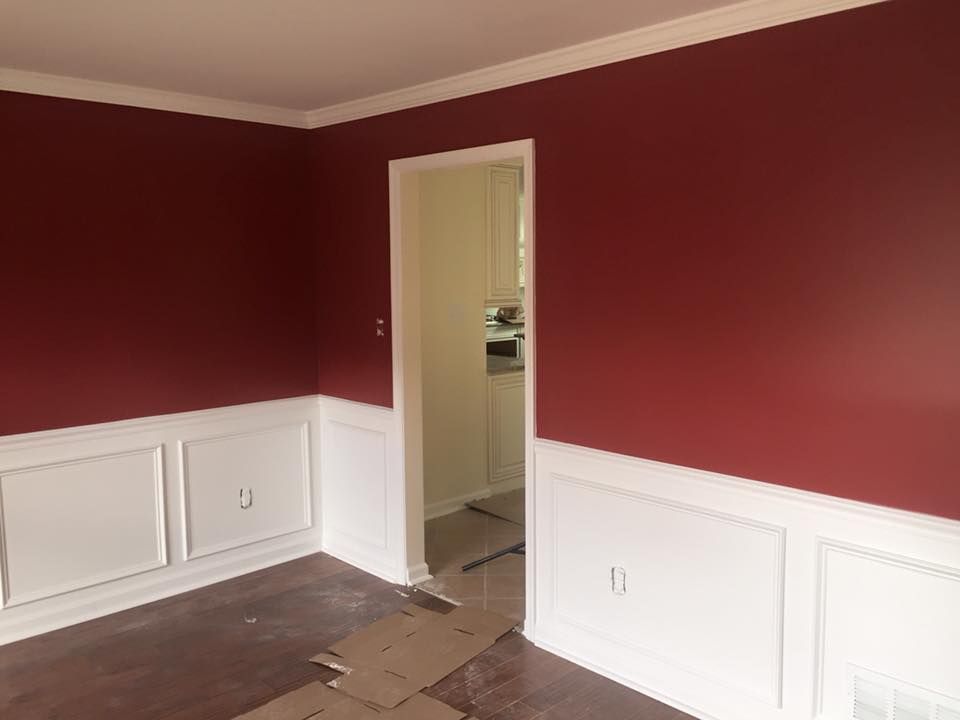 Red-painted room with white wainscoting and trim, doorway to a kitchen, and brown flooring.