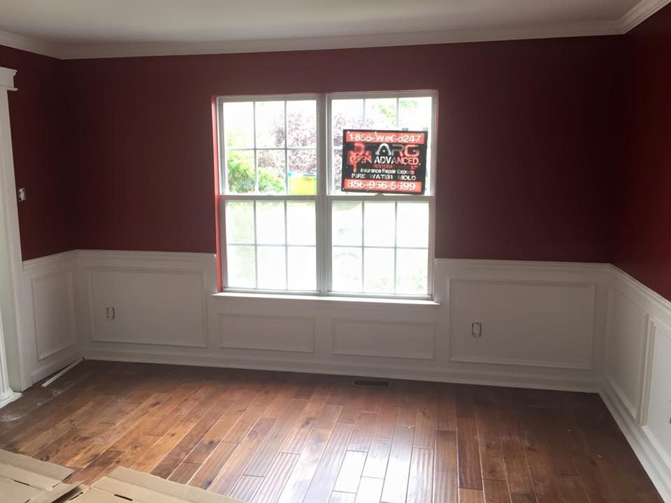 Room with burgundy walls, white wainscoting, a window, and hardwood floors.