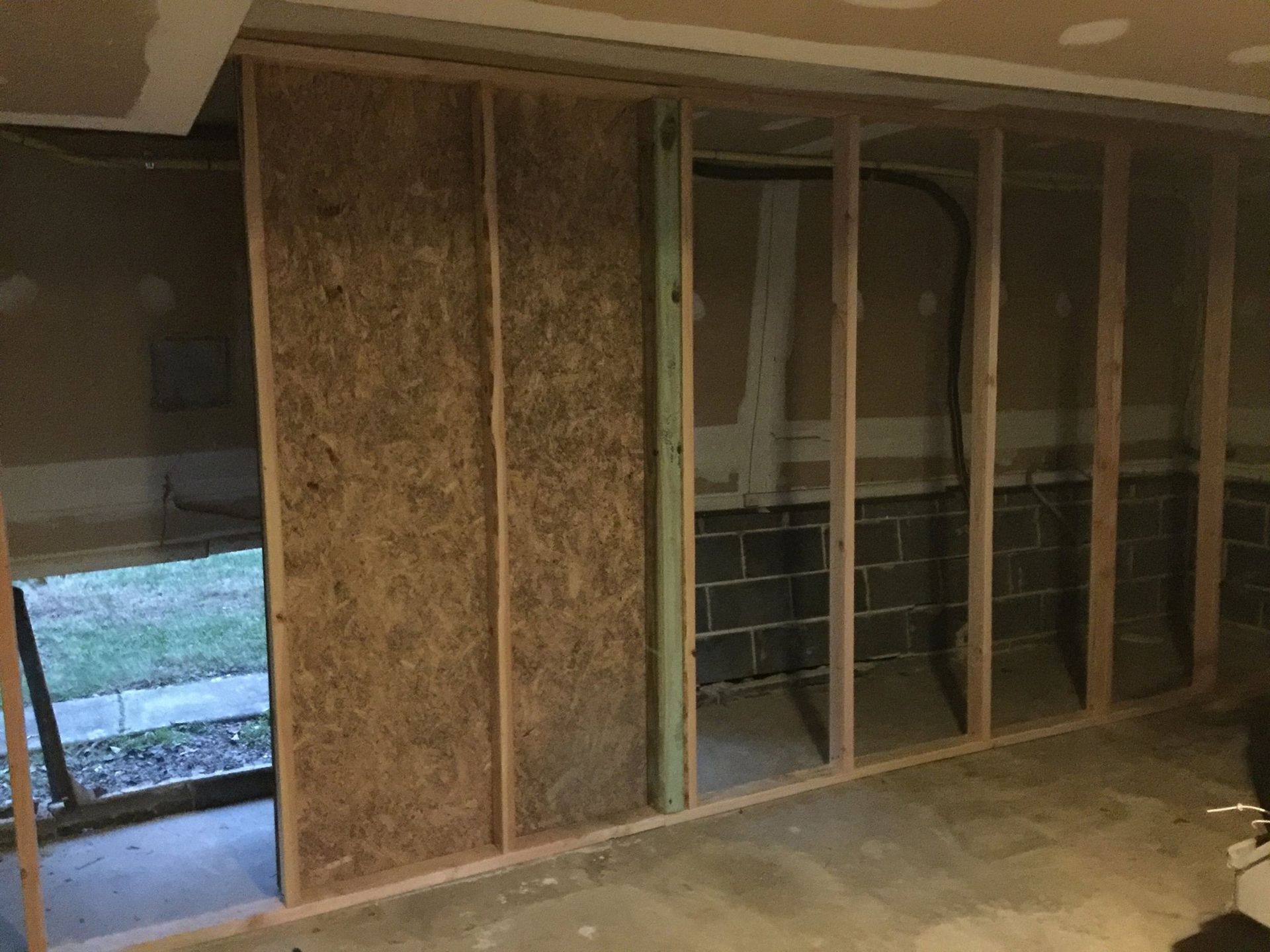 Framing of interior wall in a basement, partially covered with wood paneling; concrete floor and block wall visible.