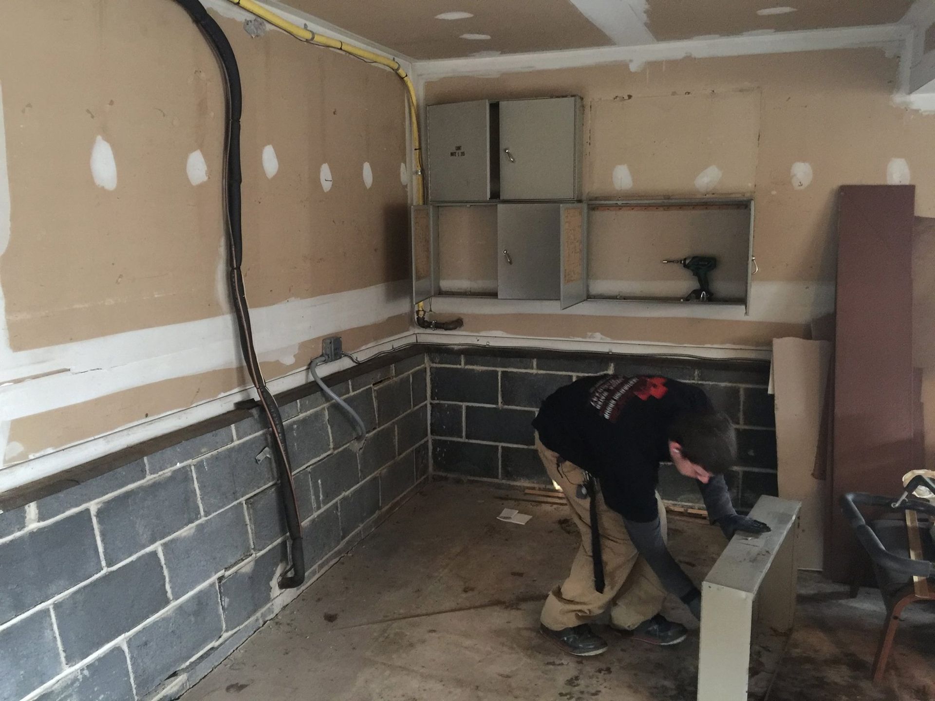 A person works on construction in a room with exposed cinder block walls and drywall.
