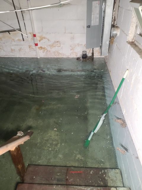 Flooded basement with standing water. Steps lead down; mop leans against a wall.