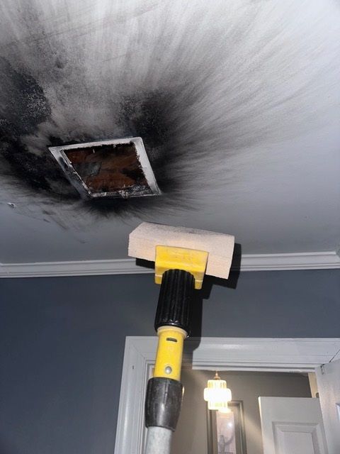 Black soot on ceiling around a vent. A cleaning tool with a yellow head is reaching towards it.