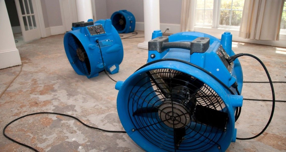 Blue air movers drying a water-damaged room with stained concrete flooring.
