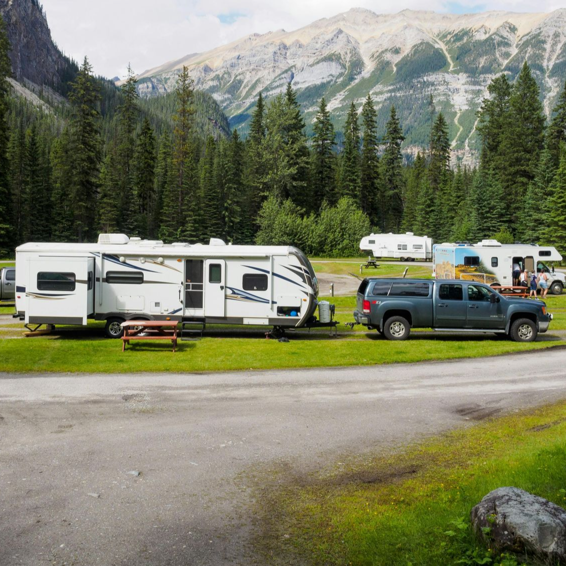 Campground with RVs parked on grass, mountains in the background, blue truck hitched to one RV.