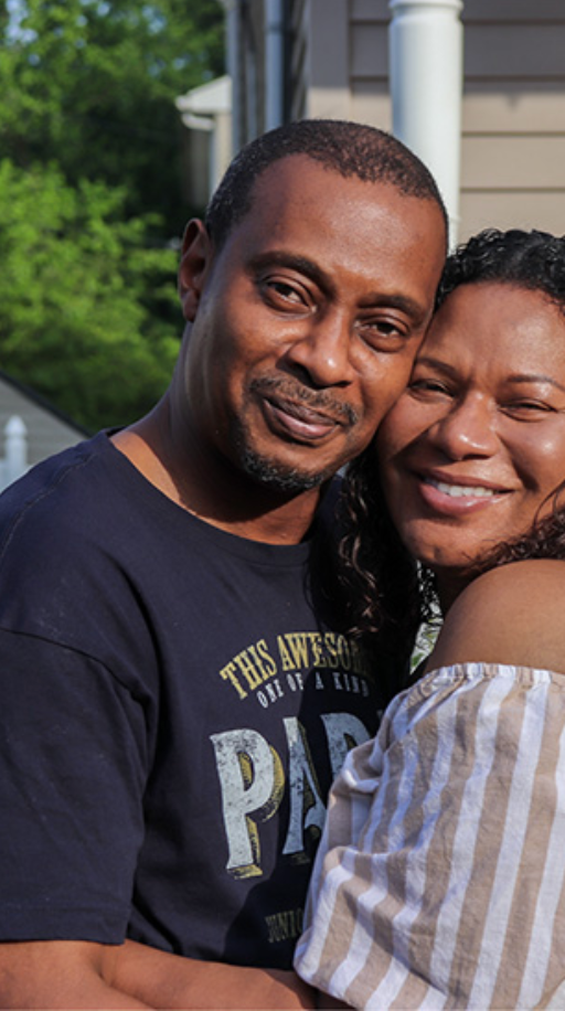 A man and a woman are hugging each other and smiling for the camera.