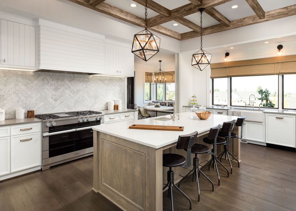 A kitchen with white cabinets , stainless steel appliances , a large island and a wooden ceiling.