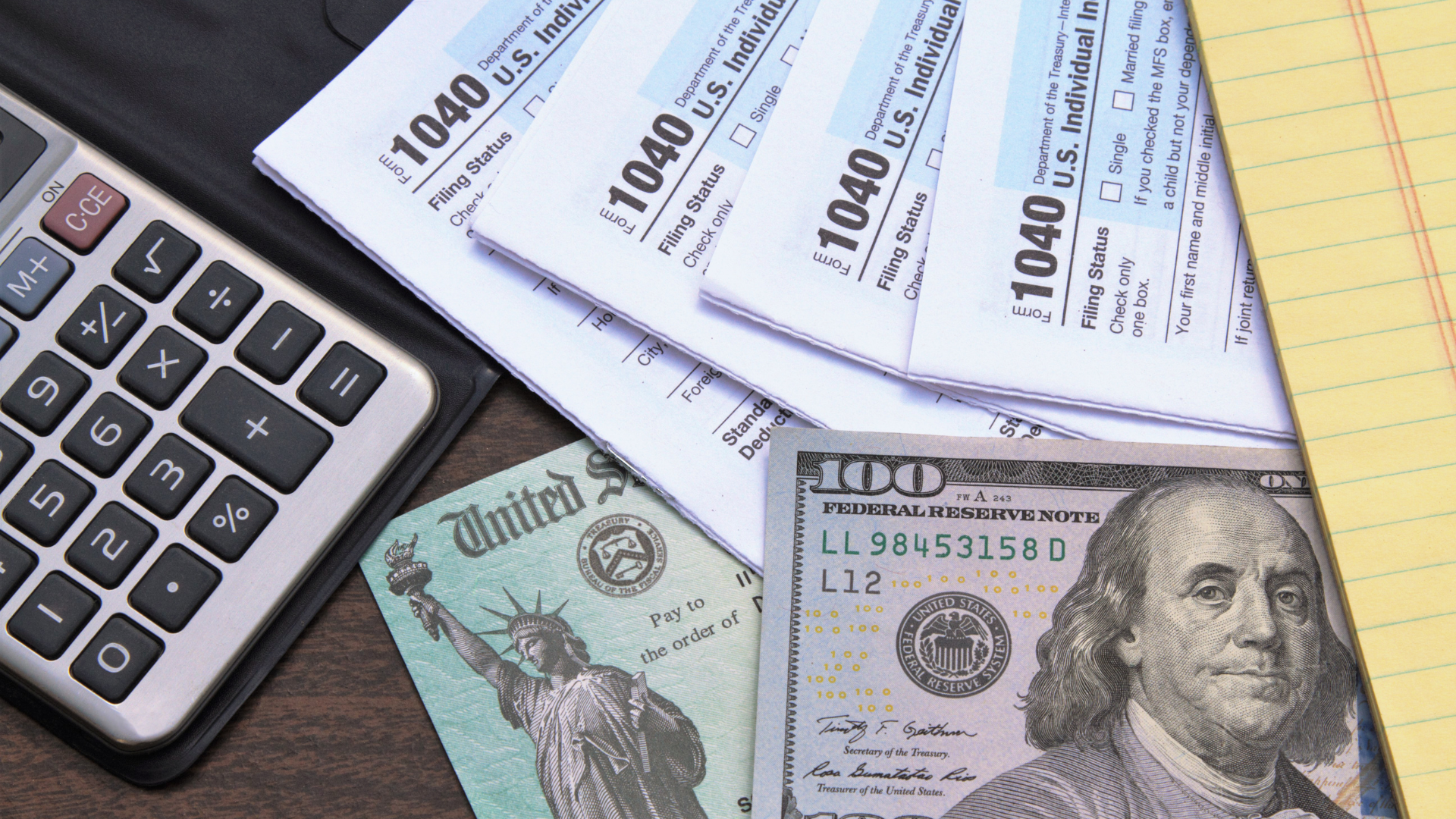 A calculator , tax forms , and a 100 dollar bill on a table