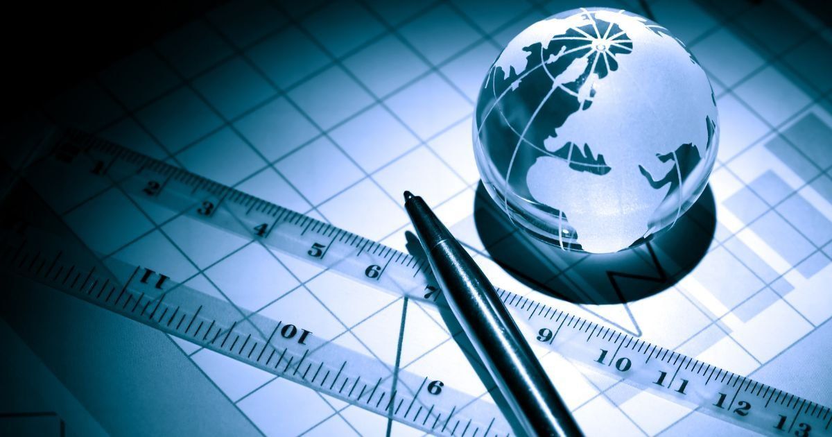 A glass globe sits atop a blueprint with a ruler and pen, all in cool blue tones, suggesting planning or global strategy.